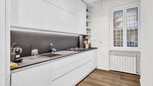 A modern kitchen with white cabinetry, a black countertop, and a built-in stove. There is a window with a view of the outside.