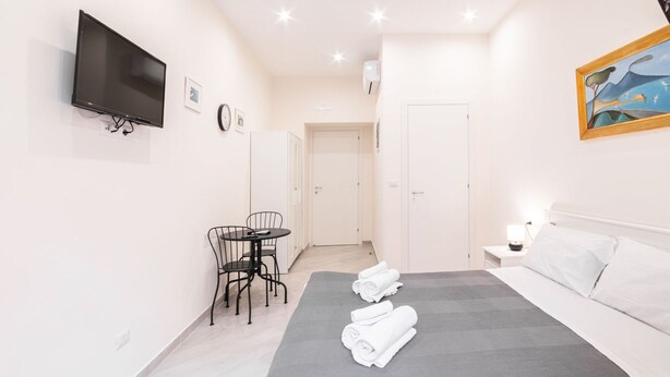 A modern hotel room with a bed, a desk, a chair, a TV, and a painting on the wall. - Dimora Sergente Maggiore By DomusExtra (Naples)