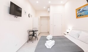A modern hotel room with a bed, a desk, a chair, a TV, and a painting on the wall. - Dimora Sergente Maggiore By DomusExtra (Naples)