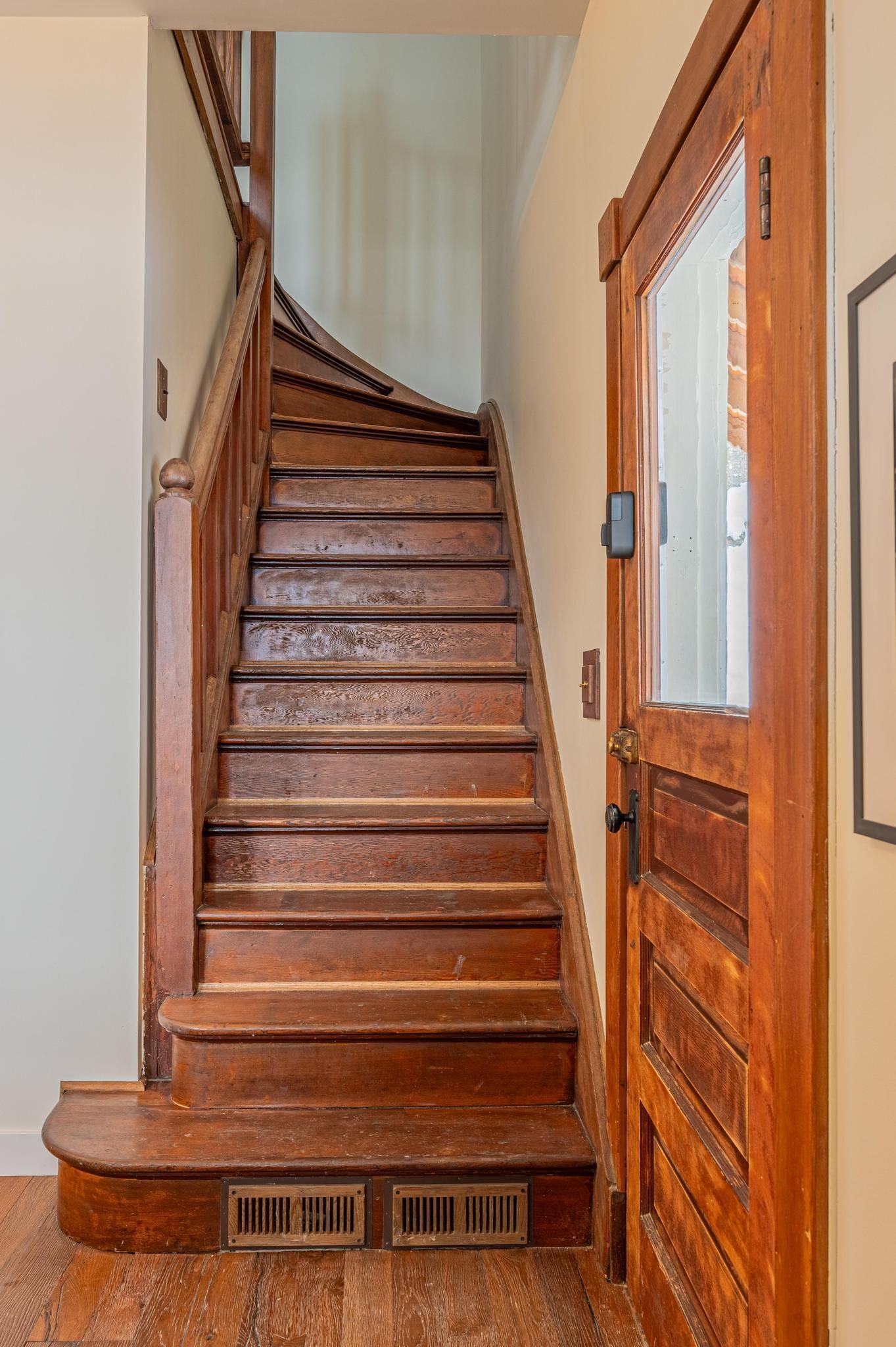 A wooden staircase with a handrail and a door with a window on the right side.