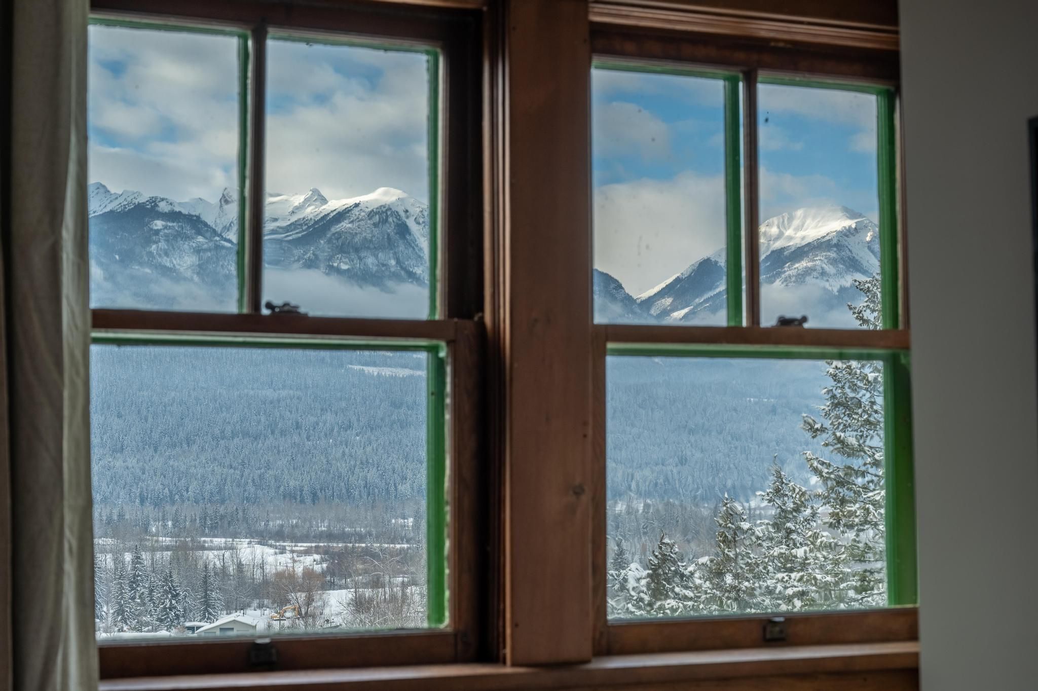 Ein Fenster mit Blick auf schneebedeckte Berge und einen bewaldeten Bereich.
