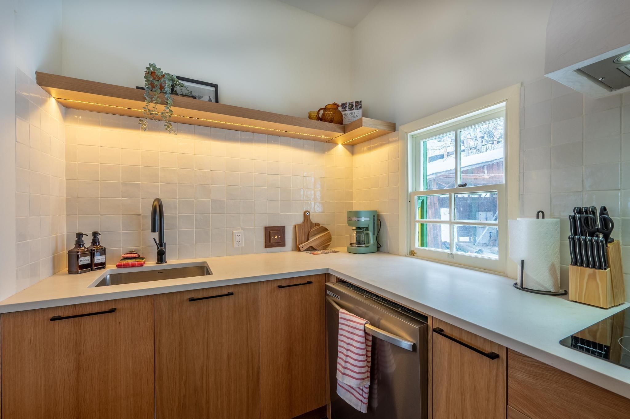 A modern kitchen with a built-in dishwasher, a coffee machine, and a window providing natural light.