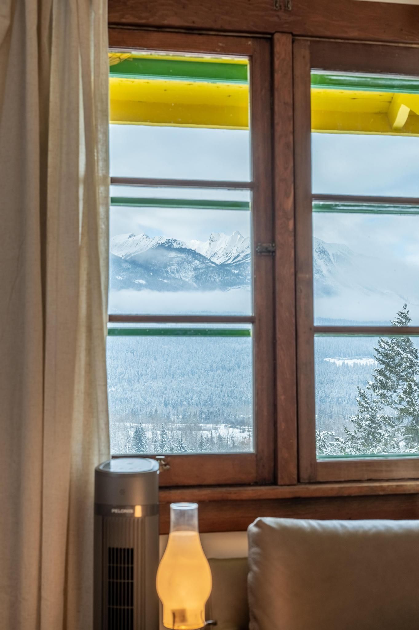Ein Fenster mit Blick auf schneebedeckte Berge und einen Wald.