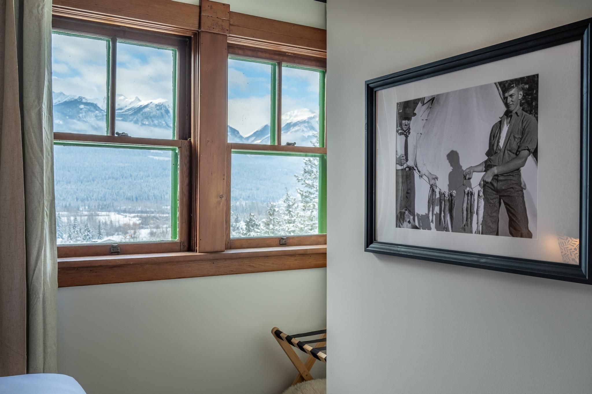 Een kamer met een groot raam dat uitzicht biedt op besneeuwde bergen en een zwart-wit foto in een lijst aan de muur.