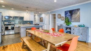 A modern kitchen with stainless steel appliances, a wooden dining table with orange chairs, and a blue accent wall. - Casa Ola Escape (St. Augustine)