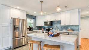 A modern kitchen with stainless steel appliances, a granite island, and pendant lighting. - Casa Ola Escape (St. Augustine)