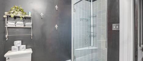 Een moderne badkamer met een douchecabine van glas, een toilet en een plank met handdoeken en toiletartikelen.