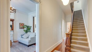 A hallway with a staircase, a white sofa, a plant, and a chandelier. - Home 2 Mi to Dtwn St Louis: Great for Families! (St. Louis)