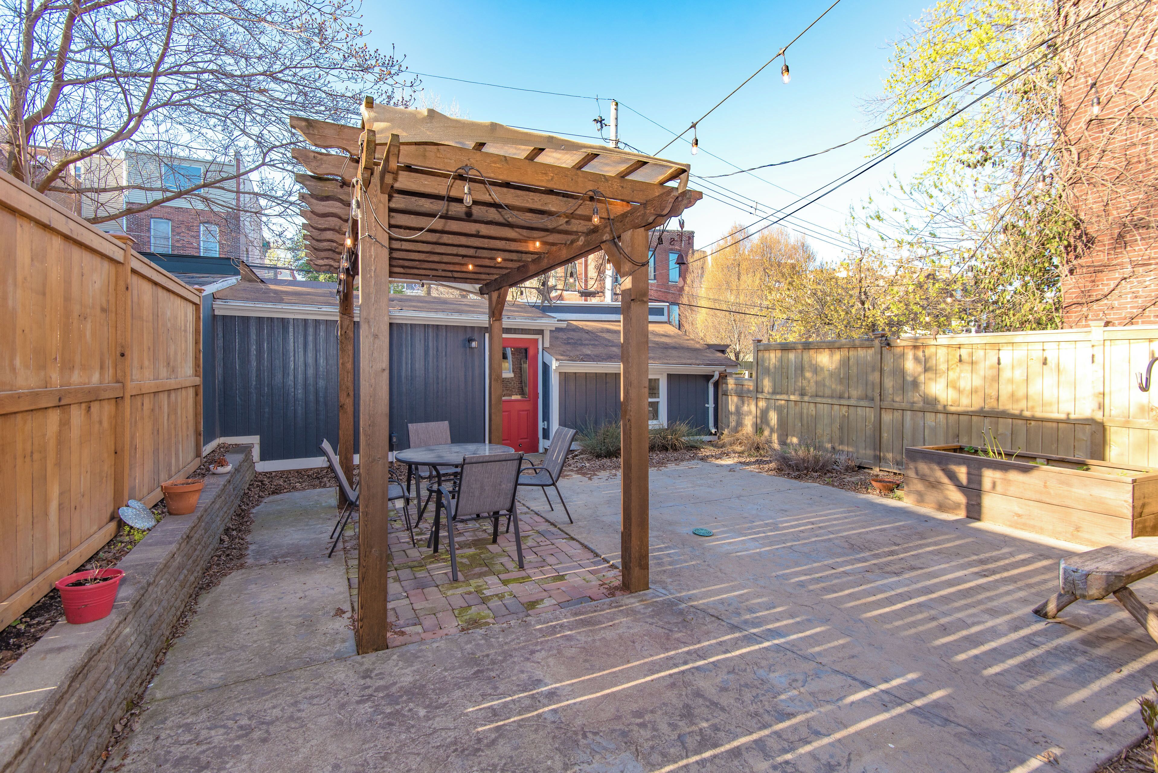 A backyard with a wooden pergola, a patio table, and chairs.