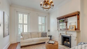 A living room with a beige sofa, a round ottoman, a fireplace, and a chandelier. - Home 2 Mi to Dtwn St Louis: Great for Families! (St. Louis)