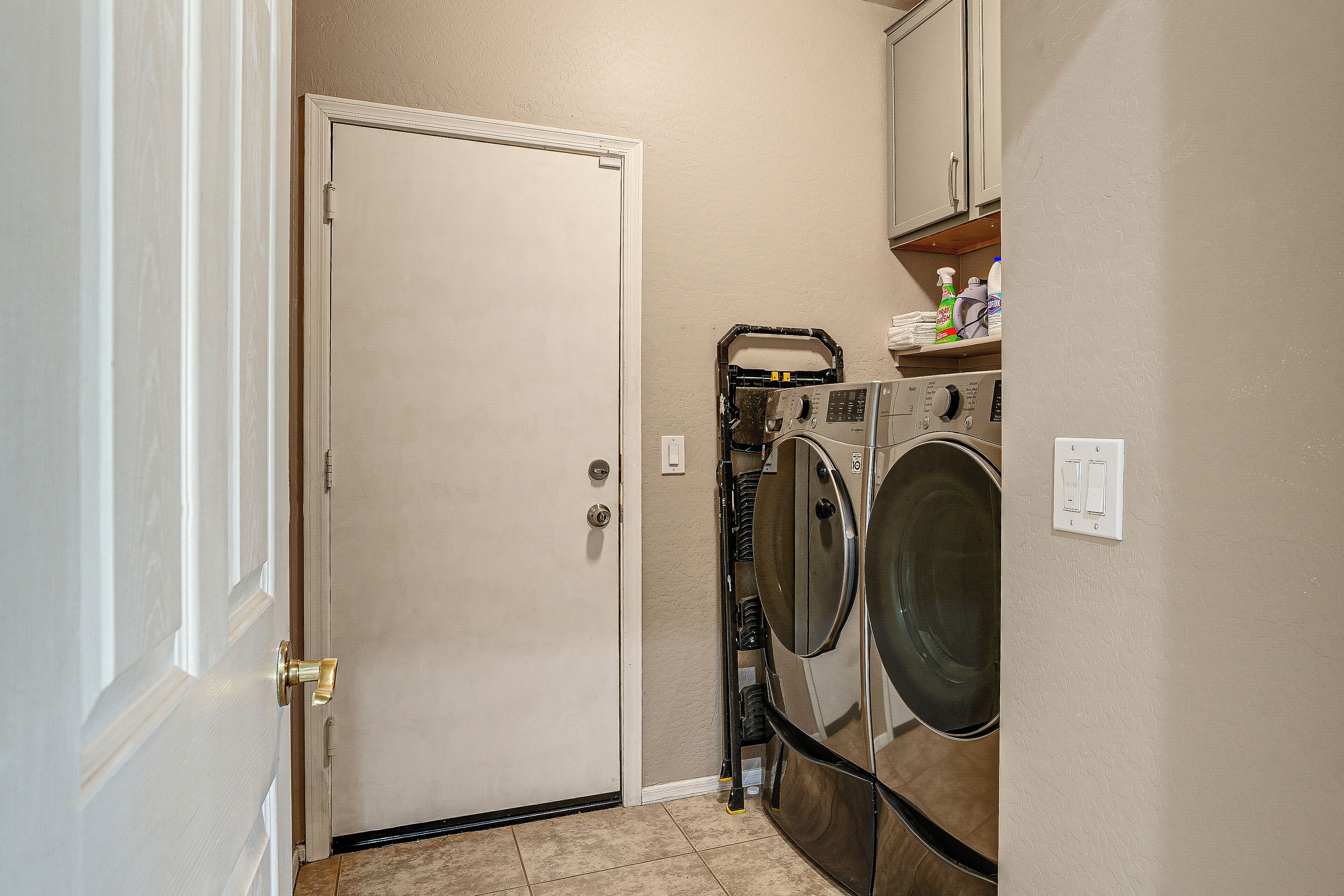 A laundry room with a closed door, a washing machine, a dryer, and a shelf with cleaning supplies.