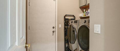 A laundry room with a closed door, a washing machine, a dryer, and a shelf with cleaning supplies.