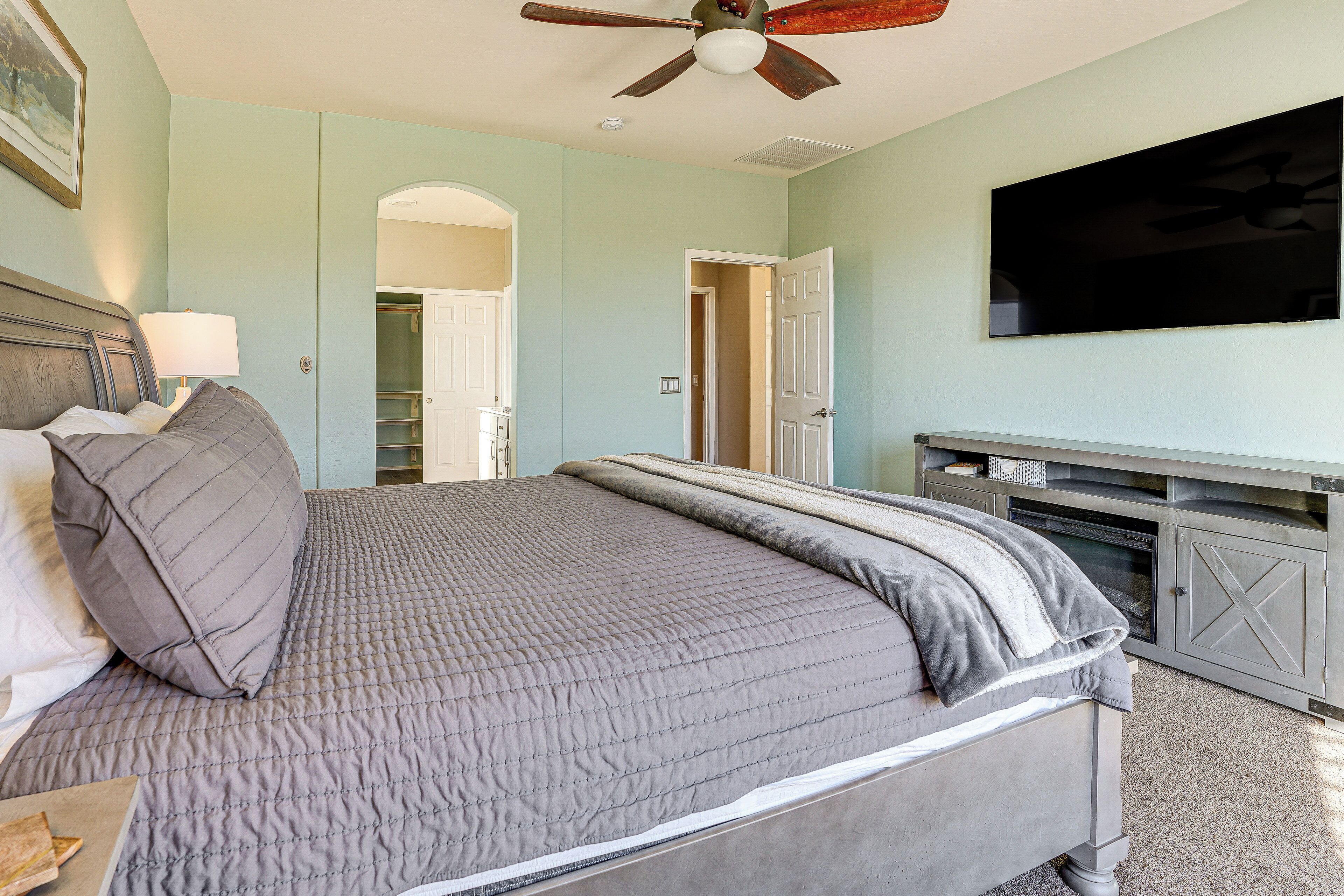 A bedroom with a bed, a ceiling fan, a TV, and a walk-in closet.