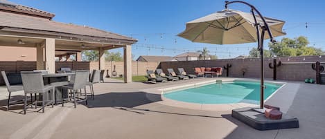 An outdoor patio with a pool, a covered dining area, and lounge chairs.