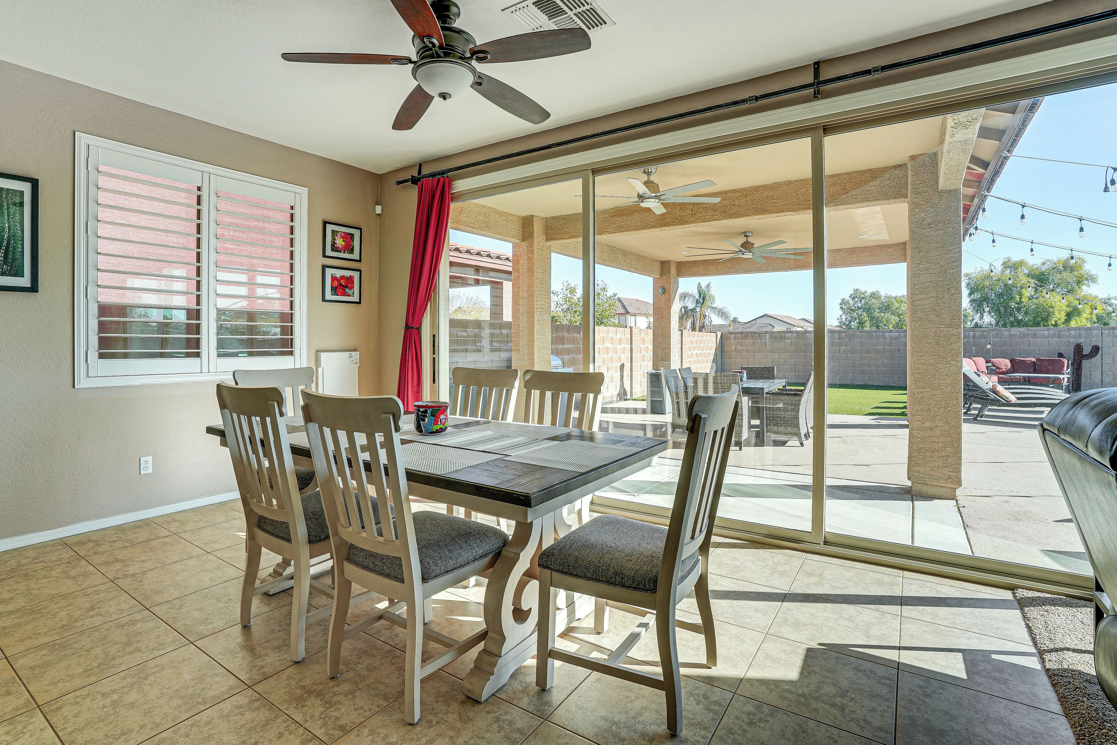 A dining area with a table and chairs, a ceiling fan, and a view through large sliding glass doors to an outdoor patio.