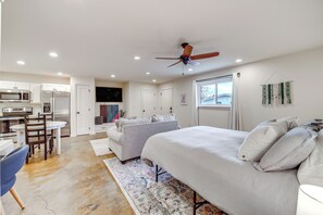 A modern kitchen with built-in appliances, a dining area with a table and chairs, a bedroom with a bed and pillows, and a ceiling fan. - Central & Modern Studio w/ Workspace in Owasso! (Owasso)