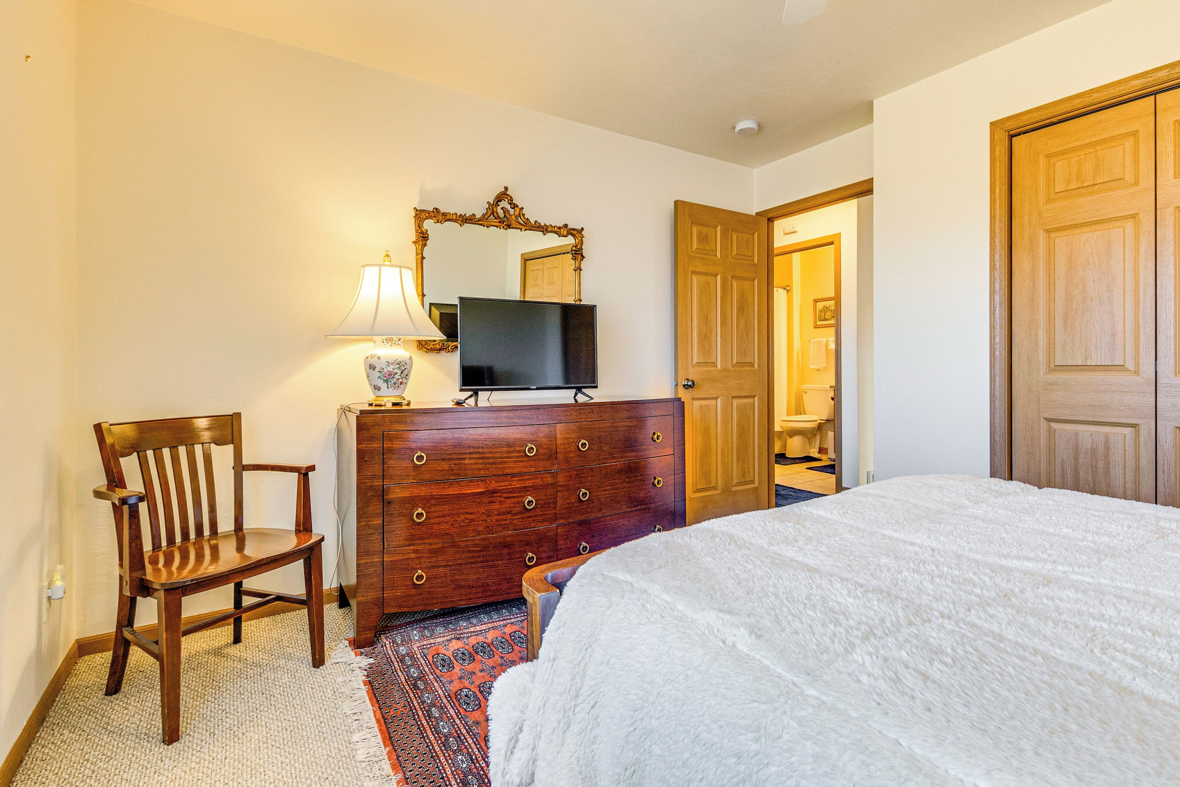 A hotel room with a bed, a wooden dresser, a television, a chair, and a door.
