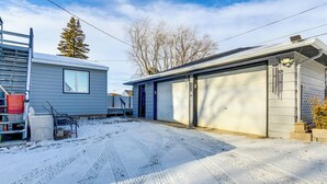 Un garage d’habitation avec une allée recouverte de neige et une échelle appuyée contre la maison.