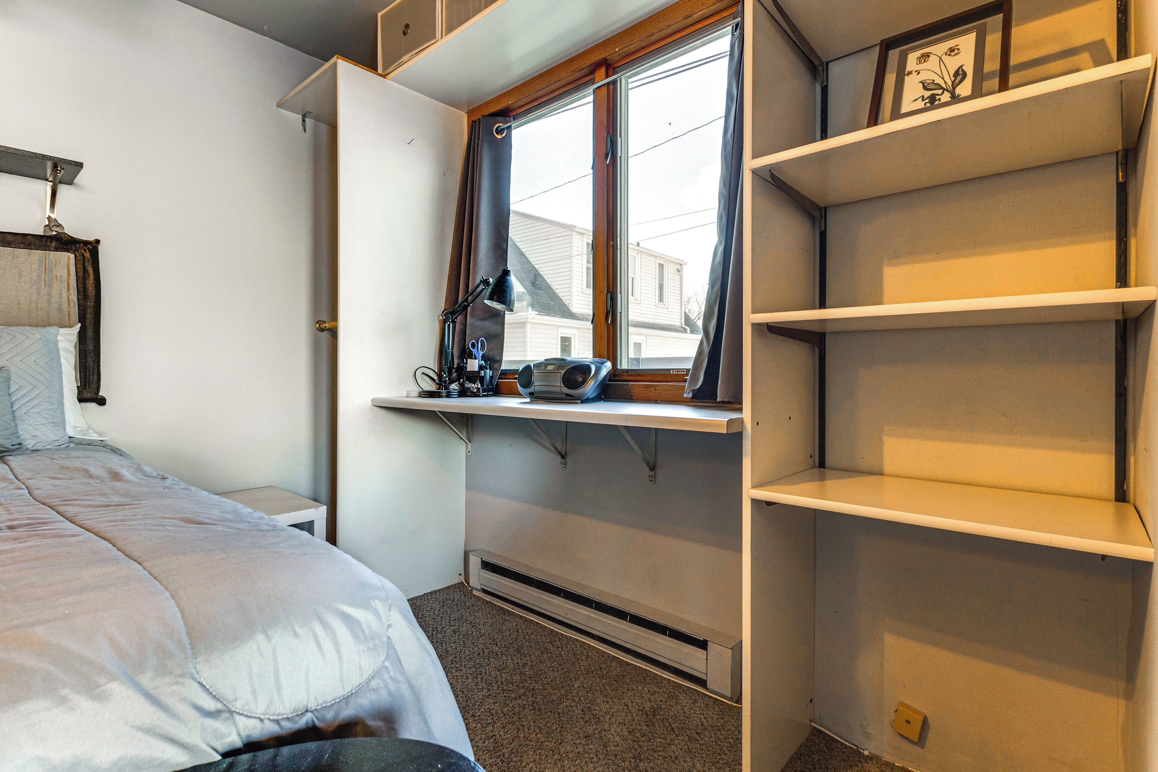 A bedroom with a bed, a desk with a computer, a window, and built-in shelves.