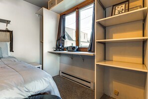 Een slaapkamer met een bed, een bureau met een computer, een raam en inbouwplanken.