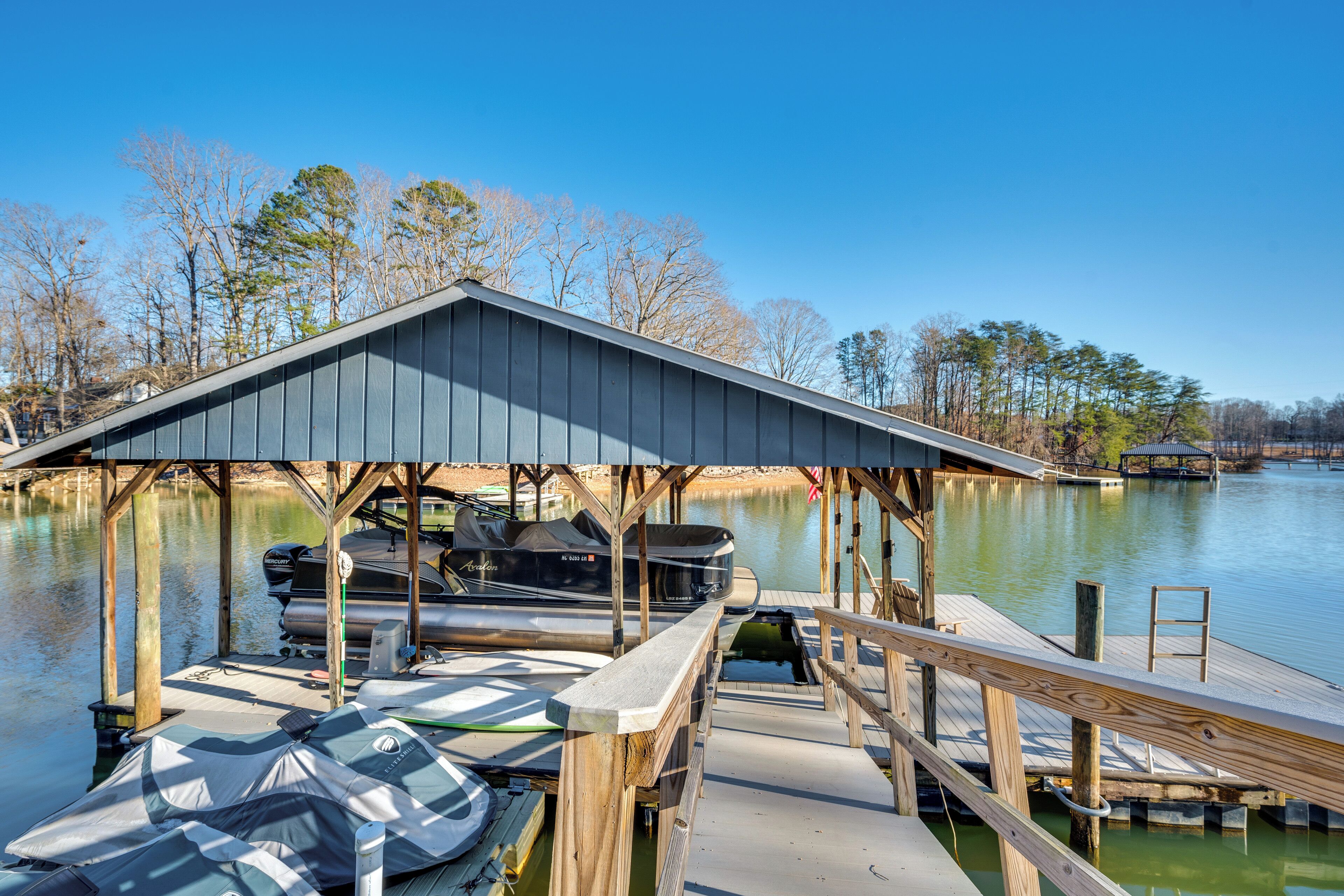 A dock with boats and a covered area, surrounded by trees and a body of water.