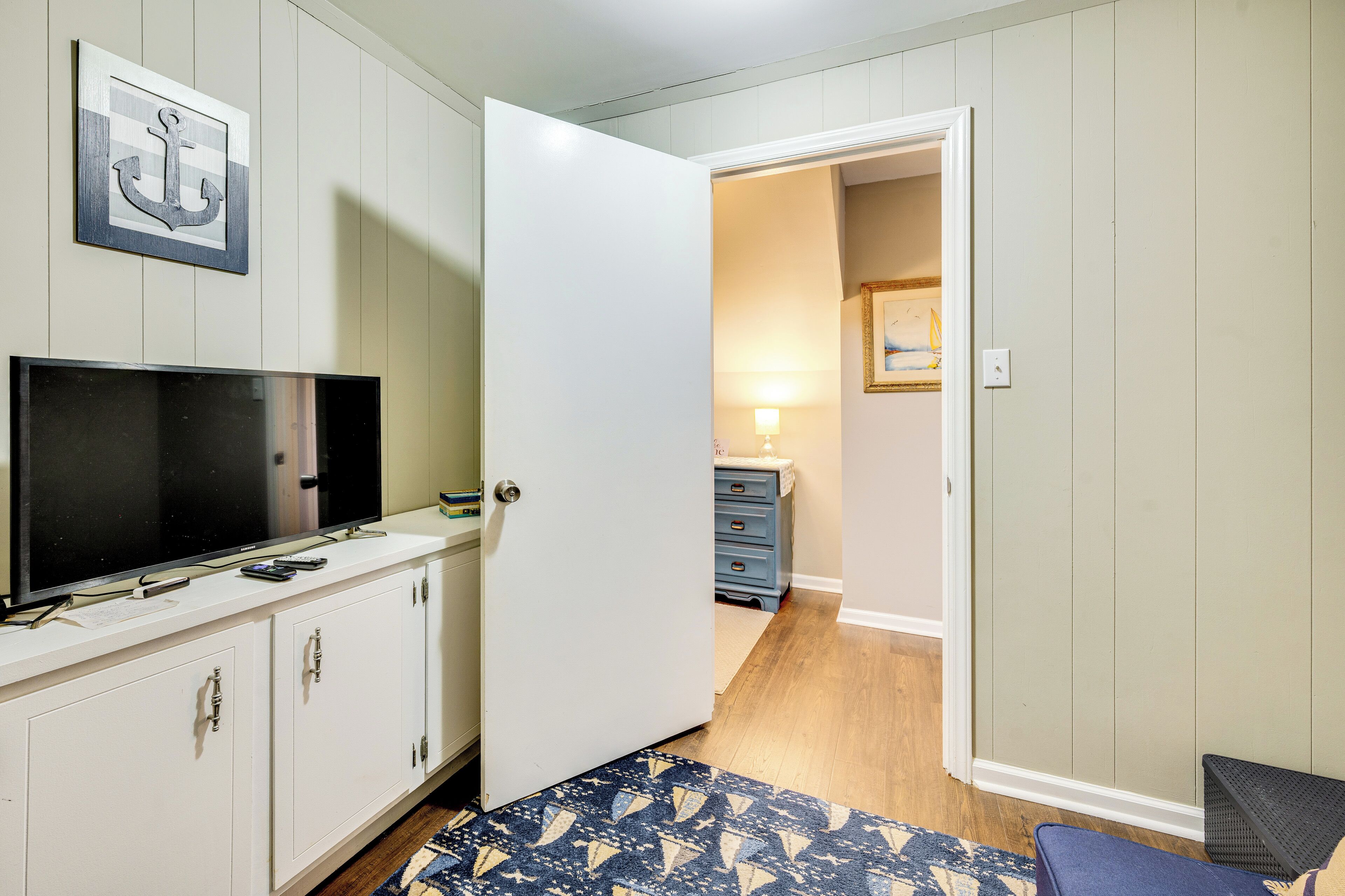 A bedroom with a TV on a white cabinet, a door leading to another room, and a patterned rug on the floor.