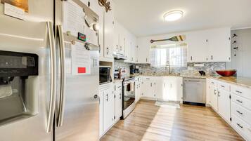 A modern kitchen with white cabinets, stainless steel appliances, and a wooden floor.