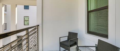 Ein Balkon mit zwei Stühlen, einem Tisch, einem Metallgeländer und einem Fenster mit Jalousien.