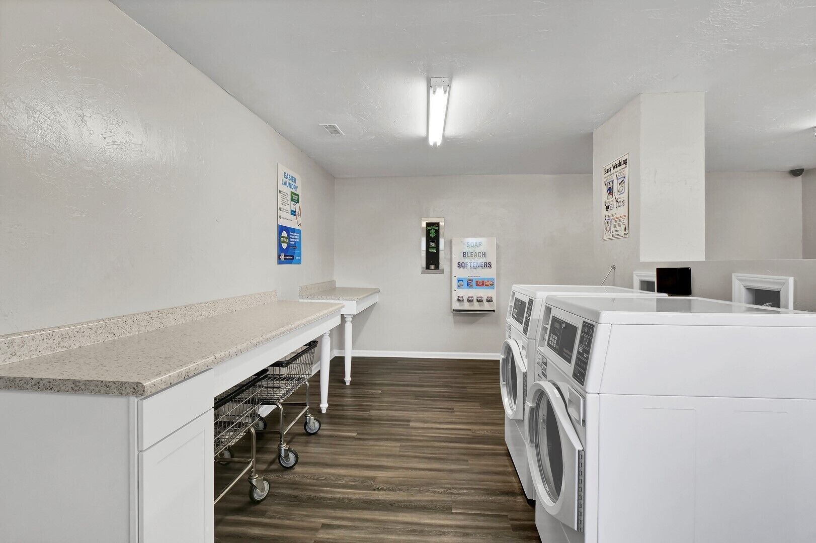 A laundry room with a countertop, washing machines, a cart, and a soap dispenser.