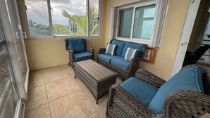 A sunlit patio with wicker furniture, a glass door, and a view of palm trees. - La Perla Azul Beach House (San Pedro)