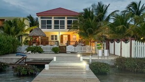 A wooden dock leading to a house with a red roof, surrounded by palm trees and a white picket fence. - La Perla Azul Beach House (San Pedro)
