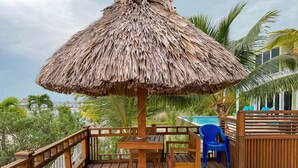 A wooden deck with a thatched umbrella, a pool, and a view of the ocean. - La Perla Azul Beach House (San Pedro)