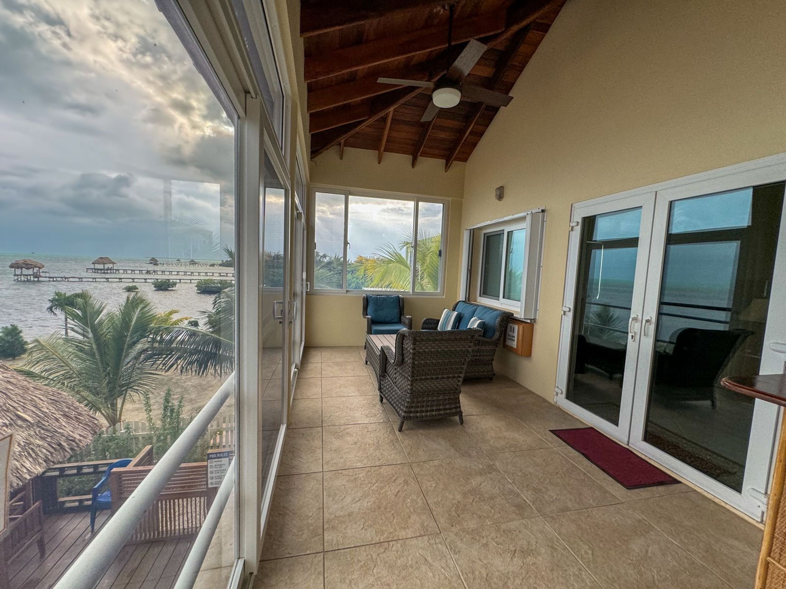 A balcony with a view of the sea, wicker furniture, and a ceiling fan.
