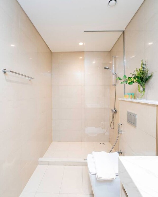 Un baño moderno con cabina de ducha de vidrio, un lavabo blanco y una planta pequeña en el mueble.