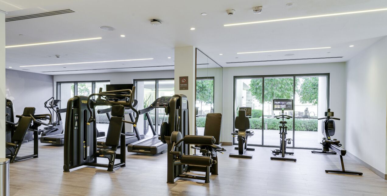 Ein modernes Fitnessstudio mit verschiedenen Trainingsgeräten, großen Fenstern und einem hellen, großzügigen Raumdesign.