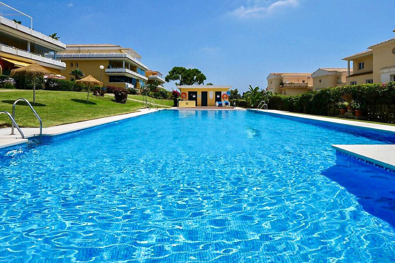 Una piscina azul cristalina rodeada de edificios con balcones y una estructura pequeña al fondo.