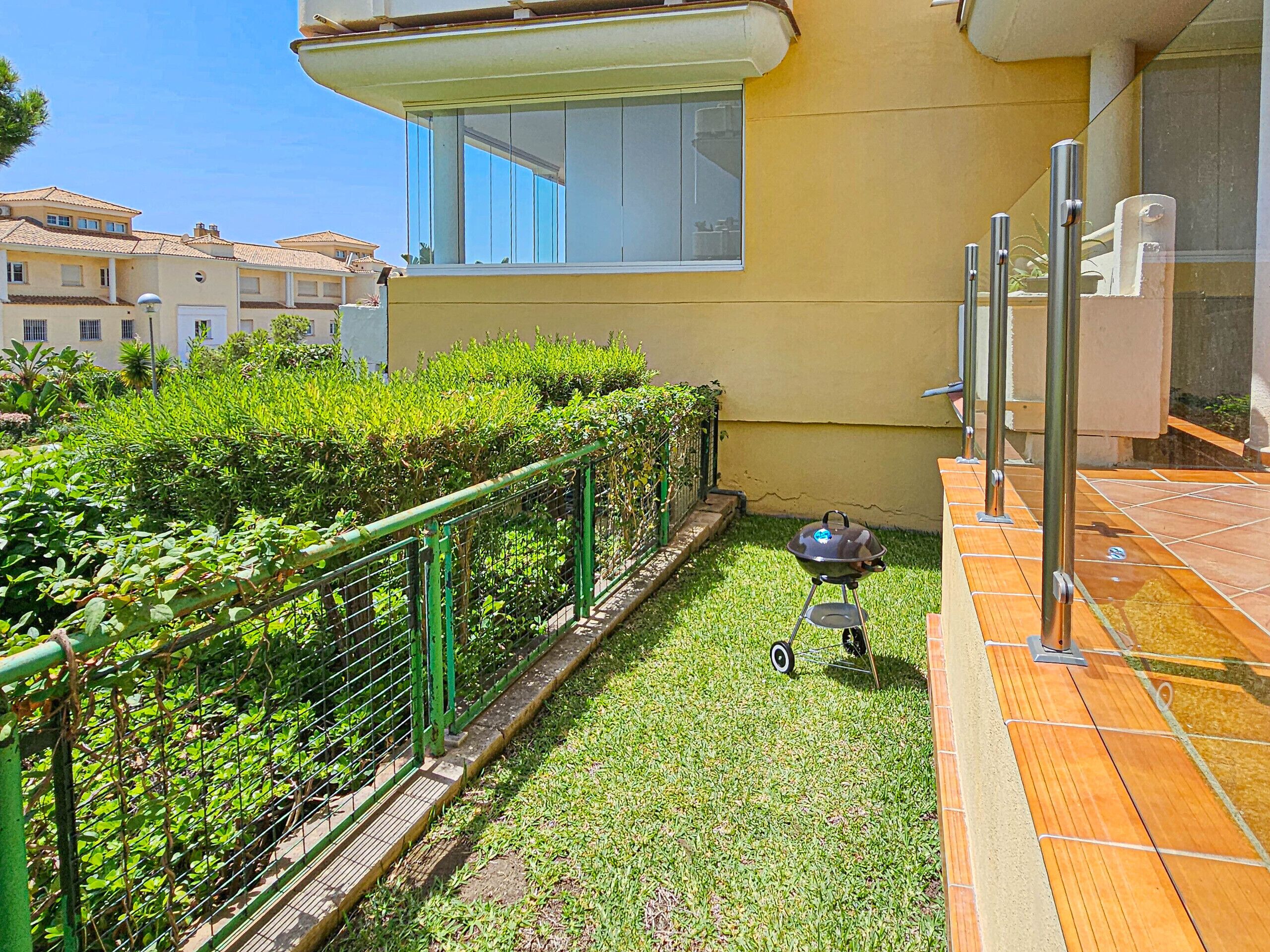 A small, fenced garden area with a grill and a tiled patio.