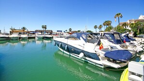 Un port de plaisance où plusieurs bateaux sont amarrés, un restaurant en arrière-plan et des palmiers bordant la côte.