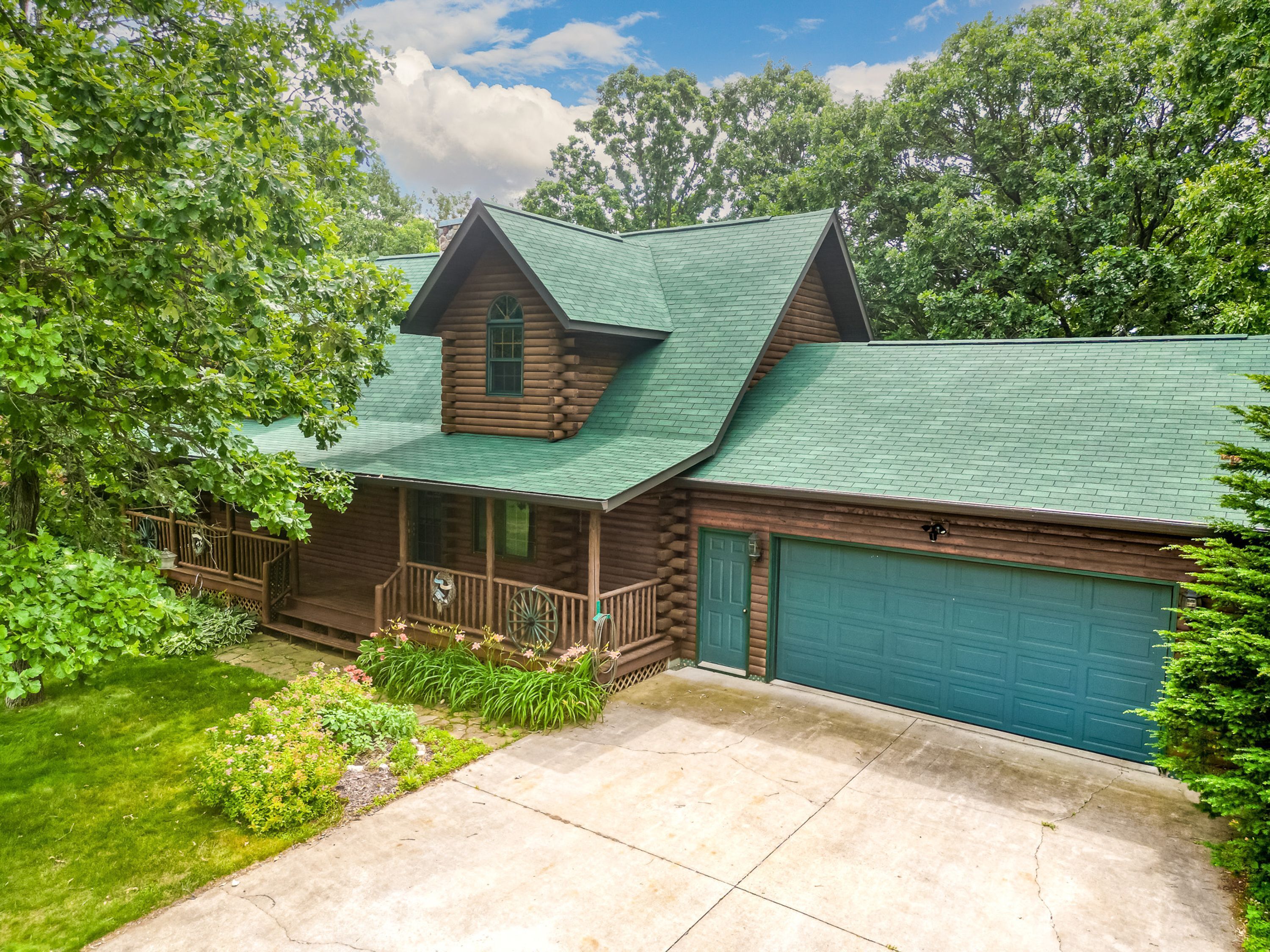 A log cabin with a green roof, a porch, and a garage.