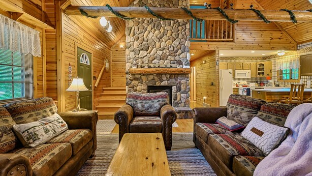 A cozy log cabin interior with a stone fireplace, wooden furniture, and a kitchen area. - Wazeecha Lodge in Wisconsin Rapids (Wisconsin Rapids)