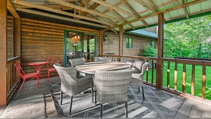 A covered patio with a wooden table and wicker chairs, surrounded by a wooden deck and railing. - Wazeecha Lodge in Wisconsin Rapids (Wisconsin Rapids)