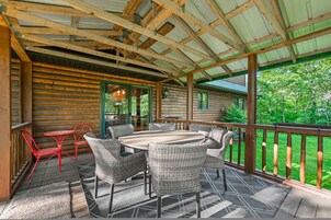 Un patio cubierto con una mesa de madera y sillas de mimbre, rodeado por una terraza y barandilla de madera.