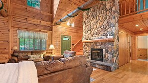 A cozy log cabin interior with a stone fireplace, wooden walls, and a comfortable seating area. - Wazeecha Lodge in Wisconsin Rapids (Wisconsin Rapids)