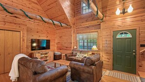 A cozy log cabin interior with a wooden ceiling, a green door, a flat-screen TV, leather sofas, and a wooden coffee table. - Wazeecha Lodge in Wisconsin Rapids (Wisconsin Rapids)