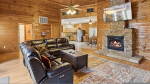 A log cabin interior with a leather sectional sofa, a fireplace, a dining area, and a kitchen. - Spectacular Home w Hot Tub Fireplace Jacuzzi (Sevierville)