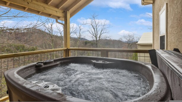 A hot tub on a covered deck with a view of trees and hills. - Spectacular Home w Hot Tub Fireplace Jacuzzi (Sevierville)