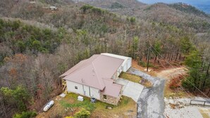 A two-story house with a red roof, surrounded by forested hills. - Spectacular Home w Hot Tub Fireplace Jacuzzi (Sevierville)