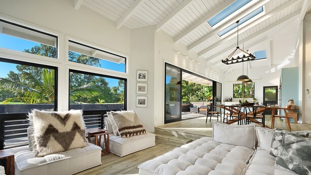 A spacious living area with large windows, a high ceiling, and a view of the outdoors. - Kamalani Modern in Princeville (Princeville)