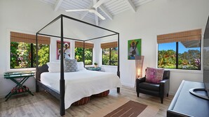 A four-poster bed with a white bedspread, a desk with a laptop, and a chair with a patterned cushion. - Kamalani Modern in Princeville (Princeville)