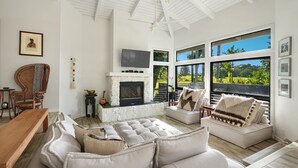 A spacious living room with a fireplace, large windows, and a high ceiling. - Kamalani Modern in Princeville (Princeville)